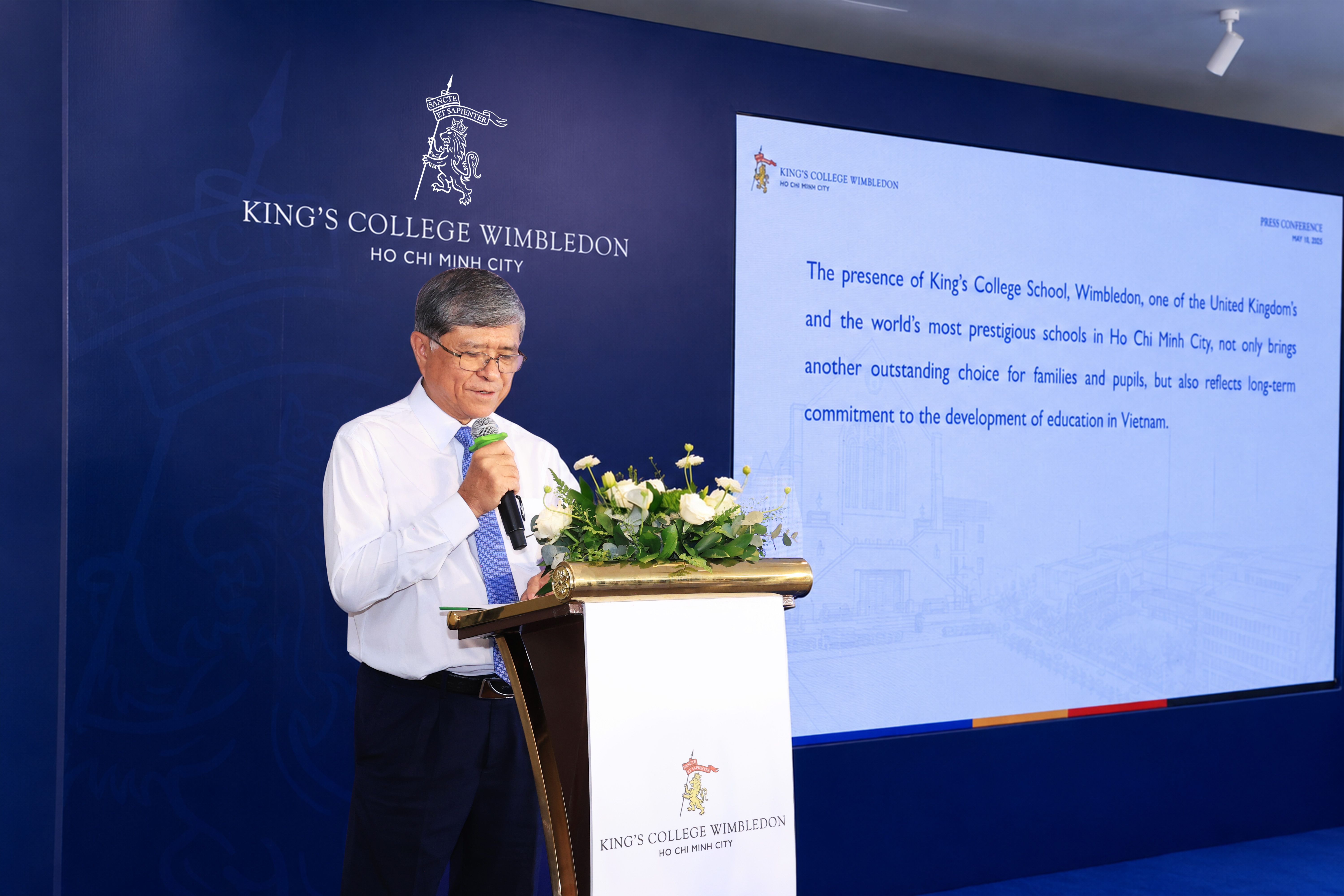 Man speaking at a podium with microphone in front of a screen displaying King's College text.