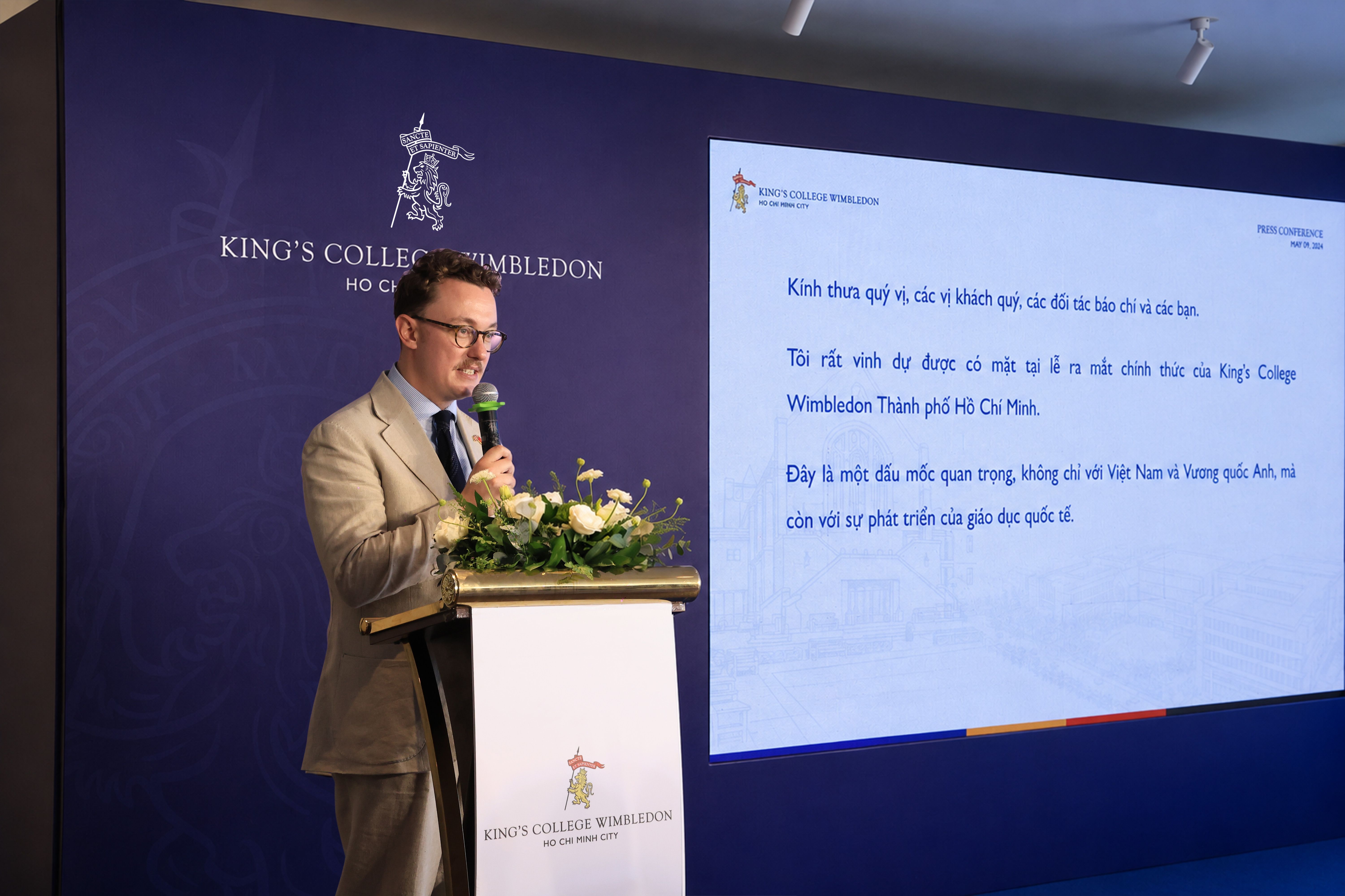 A man in a suit speaks at a podium with a microphone and presentation screen.