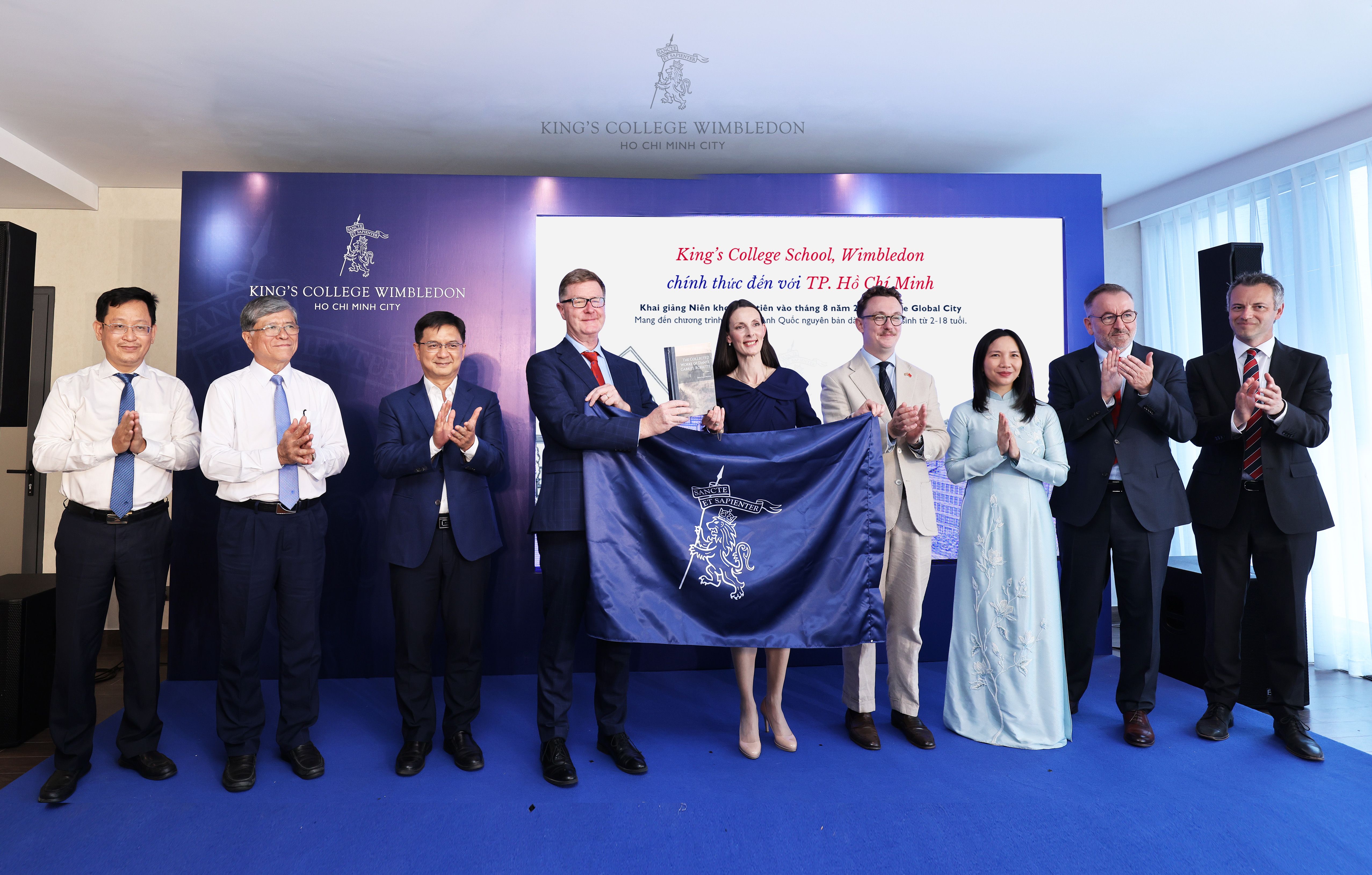 Group of officials celebrating a partnership, holding a blue flag and an award plaque.