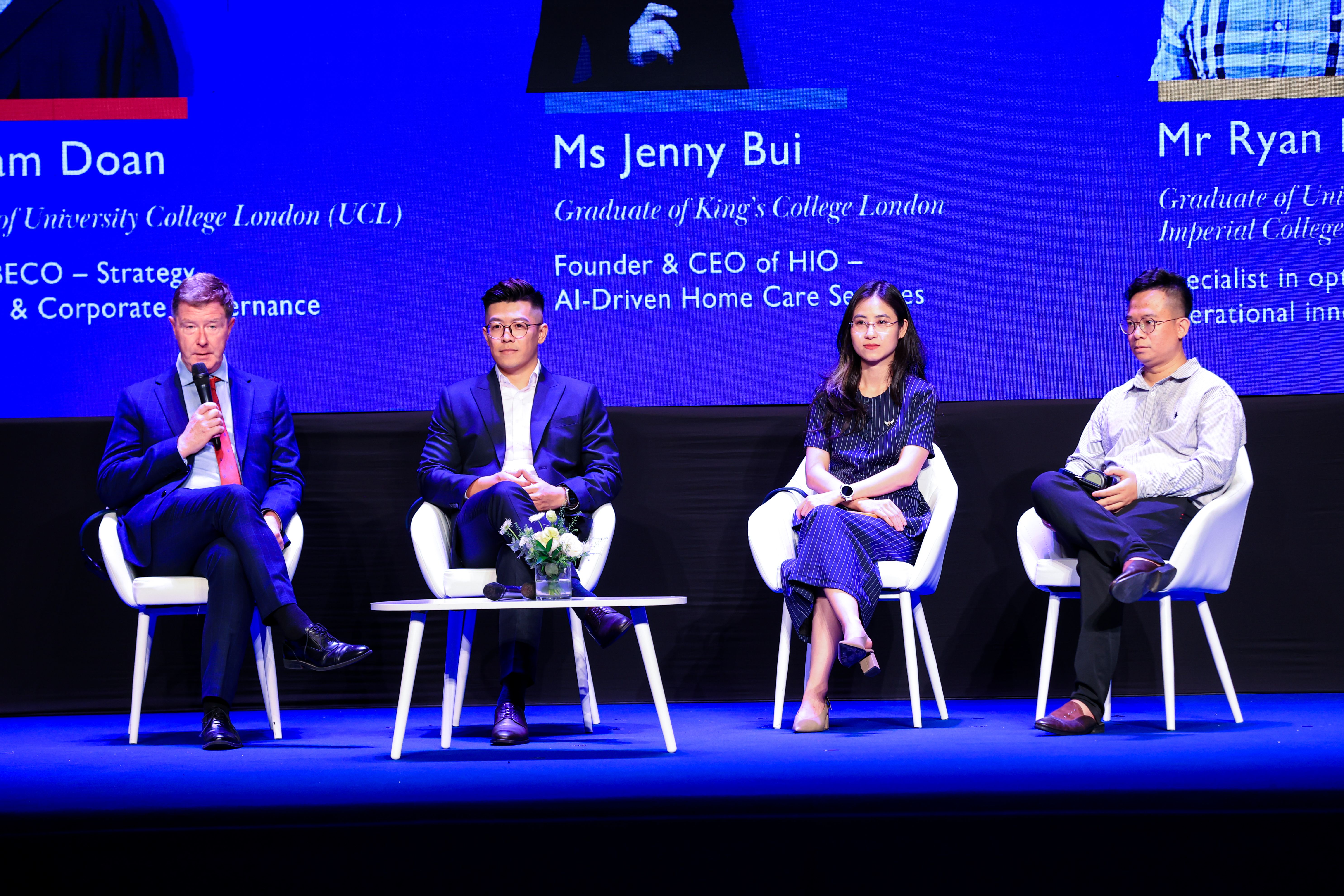 Four panelists sit on white chairs on a blue stage during a conference discussion.